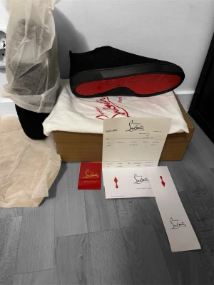 Svarta sneakers från Christian Louboutin - Säljer ett par svarta sneakers från Christian Louboutin i mocka med ikonisk röd sula. Skorna har snörning, rund tå och diskreta detaljer. Kommer med originalkartong, dustbag och certifikat. Perfekta för dig som vill ha något exklusivt och stilrent. OPS! SLUTSÅLD FÅR IN FLER OM CIRKA 15 dagar