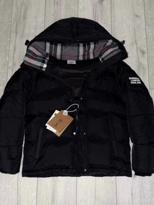 Svart pufferjacka från Burberry - Snygg svart Burberry vinterjacka i storlek S. Jackan är använd endast ett fåtal gånger och är i mycket fint skick. Klassisk och stilren design med exklusiva detaljer och hög komfort. Praktisk modell där ärmarna kan tas av, vilket gör att jackan även kan användas som väst – perfekt för både vardag och stad. Nypris betydligt högre.  Säljes nu för 2 499 kr.  💬 Pris kan diskuteras vid snabb affär. ⏳ Först till kvarn. ❓ Har du frågor är det bara att höra av dig! 📏 Storlek S.