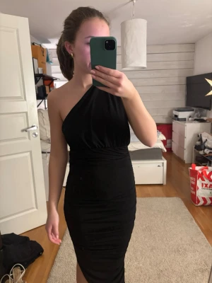 Svart one shoulder klänning NA-KD - Supersnygg svart långklänning från NA-KD x Hanna Schönberg. Klänningen har one shoulder-design och öppen rygg, vilket ger en riktigt trendig look. Sitter tight och markerar midjan. Perfekt för dig som vill sticka ut med en elegant och stilren outfit.