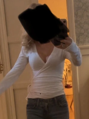 Vit omlottopp med lång ärm - Säljer en vit omlottopp med lång ärm och v-ringad hals. Toppen har snörning i sidan och är figurnära i passformen. Perfekt att styla med jeans eller kjol för en clean och fräsch look.