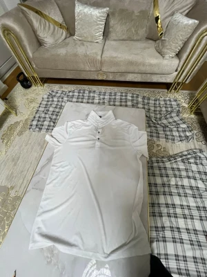 Vit polotopp med knappar - Klassisk vit polotopp med korta ärmar och tre knappar framtill. Tidlös och enkel design som passar till det mesta. Tillverkad i mjukt och lätt material som känns skönt mot huden. Perfekt för en clean och fräsch look.