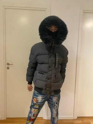 Grå pufferjacka från Zavetti - Säljer en svart pufferjacka från Zavetti med stor fluffig huva och snygga detaljer. Jackan har flera fickor framtill, dragkedja och knappar. Perfekt för kalla dagar och riktigt street i stilen.