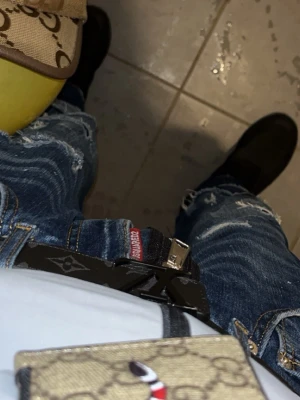 Dsquared2 blå ripped jeans - Säljer ett par blå jeans från Dsquared2 med coola slitningar och trasiga detaljer på benen. Jeansen har en mörk tvätt, klassisk femficksdesign och synliga sömmar. Passformen är normal och materialet är jeans. Perfekt för dig som gillar streetstyle.