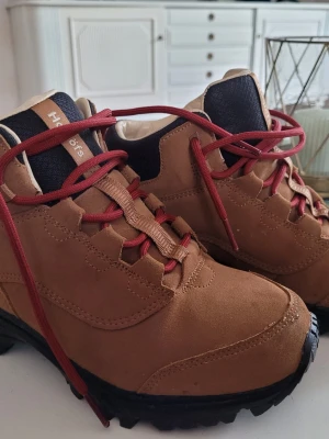 Bruna Haglöfs kängor med röd snörning - Stabila kängor från Haglöfs i brunt mocka med svarta detaljer och grov sula för bra grepp. Skorna har röd snörning och vadderad insida för extra komfort. Perfekta för utomhusaktiviteter och äventyr. Liten i storleken, skulle säga mer 37 än stl 38.