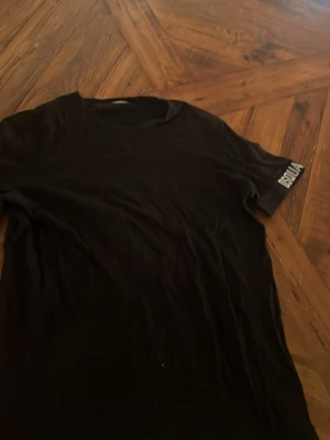 Svart t-shirt från Dsquared2 - Säljer en svart t-shirt från Dsquared2 med tryckt logga på ärmen. Klassisk passform och rund halsringning. Perfekt för dig som gillar stilrena plagg med en tydlig logga. Materialet känns mjukt och skönt mot huden.