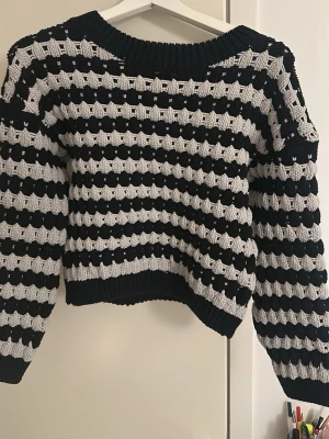 Randig stickad tröja i svart och vitt - Säljer en chunky stickad tröja med breda svarta och gråa ränder. Tröjan har en loose fit, rund halsringning och långa ärmar. Perfekt för kyliga dagar när du vill vara både bekväm och snygg.