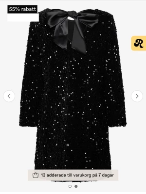 Svart paljettklänning med rosett - Supersnygg svart kortklänning täckt av glittriga paljetter och en stor satinrosett i nacken. Klänningen har lång ärm och rak passform, perfekt för dig som vill sticka ut. Materialet känns lyxigt och skimrar i ljuset.