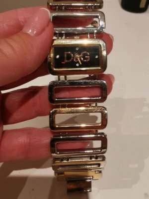 D&G klocka i silver och guld - Säljer en unik D&G klocka i silver och guld.  OBS! Att bilderna är lånade men den är i samma skick, det finns en skada längst ner på kedjan men inget som påverkar eller syns då det är på undersidan när man har på sig den. Om ni har frågor dma mig! Pris kan diskuteras vid snabb affär!