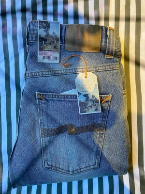 Nudie Jeans Grim Tim Silver Indigo W31 L30 - Säljer ett par Nudie Jeans Grim Tim i tvätten Silver Indigo. Klassiska blå jeans med raka ben, orange sömmar och bakfickor med Nudie-signatur. Tillverkade av 100% ekologisk bomull för en schysst känsla och look. Helt oanvända!
