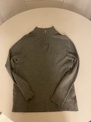 Kashmir quarter zip - Säljer en grå stickad tröja med ribbad krage och muddar. Tröjan har en snygg half zip-dragkedja vid halsen och är långärmad. Perfekt för dig som gillar enkel och stilren design med lite sportig touch.