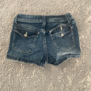 Mörkblå jeansshorts från H&M - Säljer ett par mörkblå jeansshorts från H&M med klassisk femficksdesign, uppvikta benslut och snygga detaljer, silverfärgade knappar. Perfekta till sommaren och lätta att matcha med allt.