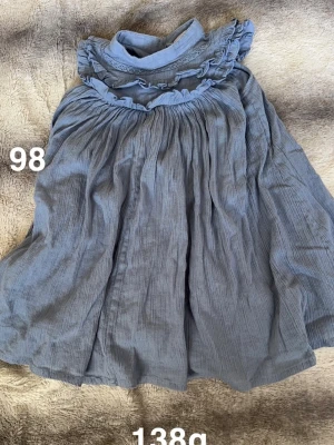 Blå volangklänning med hög krage - Supersöt blå klänning med volanger och hög krage. Klänningen har ett luftigt fall. Perfekt för dig som gillar romantiska detaljer och en avslappnad look.🌸 Fint använt skick. Storlek 98 