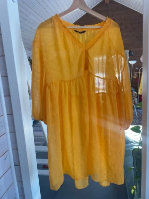 Gul klänning från KappAhl - Säljer en superfin gul kortklänning från KappAhl med v-ringning och trekvartsärm. Klänningen har en luftig, lätt struktur och volangdetaljer vid halsringningen och ärmsluten. Perfekt för soliga dagar och ger en riktigt glad vibe!