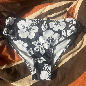 Svart och vit blommig bikiniunderdel S - Säljer en svart och vit bikiniunderdel från Temu i storlek S. Den har ett stort blommigt mönster och snörning i sidorna för justerbar passform. Materialet är mjuk polyester med elastan som ger bra stretch och komfort. Perfekt för strandhäng!