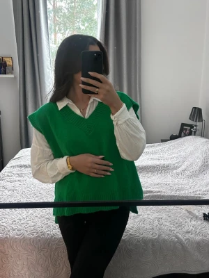 Grön stickad väst med v-ringning - Säljer en grön stickad väst  med v-ringning och breda ribbade kanter. Västen har en loose passform och är perfekt att styla över en skjorta. Enkel och stilren design som ger en cool touch till outfiten.