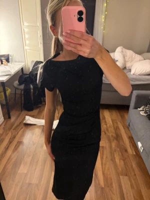 Svart tight långklänning Kappahl  - Helt ny med prislapp på ordinarie pris 499kr Säljer en svart långklänning med korta ärmar och figurnära passform. Klänningen har en enkel och stilren design utan mönster eller detaljer, perfekt för dig som gillar en klassisk look. Materialet känns mjukt och följsamt mot kroppen.