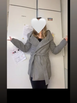 Grå kappa med bälte  - Säljer en snygg grå kappa med stora slag och bälte i midjan. Jackan har knappar framtill. Perfekt för dig som vill ha en stilren och enkel look till höst och vinter.