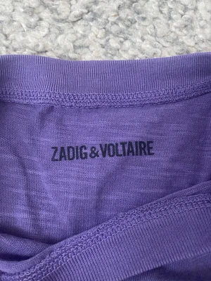 Lila Zadig & Voltaire tour t-shirt - Säljer en lila Zadig & Voltaire t-shirt med coolt tour-tryck både fram och bak. Framsidan har ett grafiskt motiv med vingar och texten 'ART IS TRUTH', medan baksidan visar turnédatum. T-shirten är ärmlös och i mjuk bomull. Priset kan diskuteras 💞