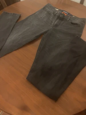 Svarta jeans från Alberto W32 L36 - Snygga svarta jeans från Alberto med klassisk femficksdesign och coola detaljer på bakfickorna. Jeansen är tillverkade i bomull med lite elastan för extra komfort och har raka ben. Perfekta till en avslappnad stil.