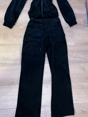 Svart velourtröja och byxor med dragkedja - Säljer en svart velourtröja med huva och dragkedja framtill. Tjocktröjan har en mjuk känsla, fickor på sidorna och en enkel, stilren look. Perfekt för dig som gillar en chill och avslappnad stil. Får även med byxor som är utsvängda.