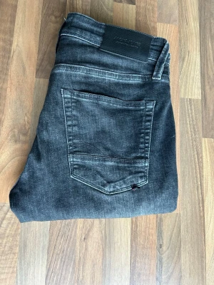 Jack & Jones svarta jeans Glenn  - Säljer ett par svarta jeans från Jack & Jones, modell Glenn. Jeansen har en snygg tvättad look med klassiska fem fickor och bälteshällor. Materialet är mjukt och stretchigt jeans-tyg som sitter skönt. Spot-on för dig som gillar stilrena och moderna jeans.