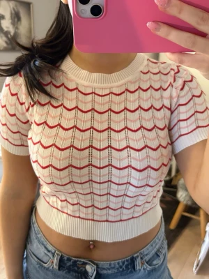 Vit och röd ribbad croppad topp - Säljer en croppad topp i vitt med röda vågiga ränder. Toppen har korta ärmar, rund halsringning och är ribbad i materialet. Perfekt till jeans eller kjol för en chill och trendig look.