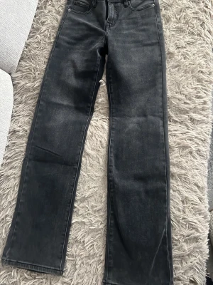 Svarta raka jeans - Säljer ett par svarta jeans med rak passform och klassisk femficksdesign. Jeansen har en något tvättad look och är tillverkade i ett slitstarkt denimtyg. Perfekta till sneakers eller boots för en clean och enkel stil.