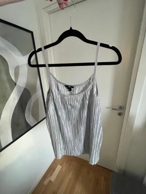 Silverfärgad linnetopp H&M - En glansig, plisserad linnetopp från H&M i silver. Toppen har tunna axelband och ett luftigt, flowy fall
