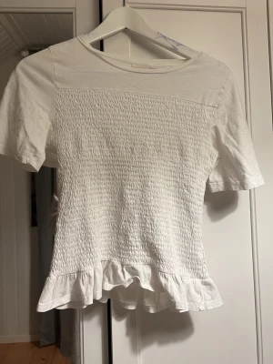 Vit topp med volangkant - Säljer en söt vit topp med korta ärmar och smockad framsida. Toppen har en volangkant. storlek 170