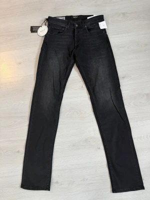 Replay 573 Bio svarta jeans, W30 L34 - Svarta Replay 573 Bio jeans med klassisk femficksdesign och raka ben. Jeansen är tillverkade i ekologisk bomull och har en snygg, mörk tvätt. Märkespatch bak i midjan och etikett på fickan. Perfekta för dig som gillar stilrena och bekväma jeans.