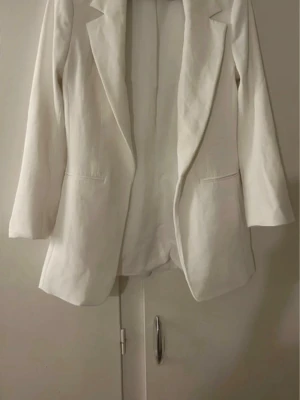 Vit kavaj från H&M, storlek 34 - Säljer en stilren vit kavaj från H&M i storlek 34. Klassisk modell med långa ärmar, spetsiga slag och två fickor framtill. Perfekt för dig som vill ha en clean och fräsch look. Materialet känns mjukt och har en lätt struktur.