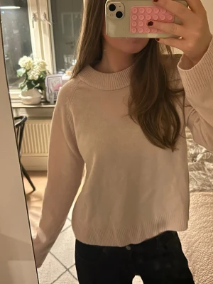 Ljusrosa stickad tröja - Mysig ljusrosa stickad tröja med bred ribbad krage och långa ärmar. Tröjan har en relaxed passform och ribbade muddar vid ärmslut och nederkant. Perfekt för lager på lager under kyliga dagar.