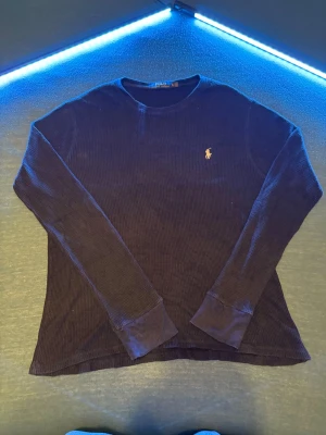Mörkblå långärmad tröja Polo Ralph Lauren - Mörkblå långärmad tröja från Polo Ralph Lauren i ribbad bomull. Klassisk rund hals och ikonisk broderad logga på bröstet. Perfekt till chill outfits och enkel att matcha med jeans eller cargos. Fläckar finns men går nog att tvätta bort