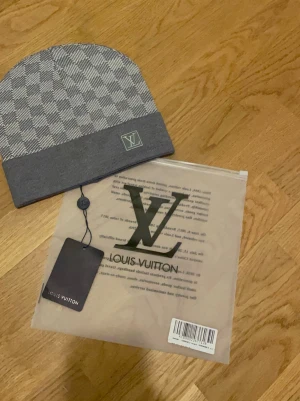 Grå rutig LV sett - Snygg grå sett från Louis Vuitton med klassiskt rutigt mönster och vikt kant. LV-logga framtill. Perfekt accessoar för dig som vill ha en exklusiv touch på din outfit.