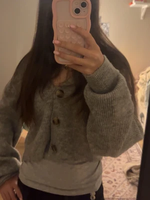 Grå kofta från H&M med stora knappar - Mysig grå kofta från H&M i storlek M. Koftan är stickad med stora, synliga knappar framtill och har en loose passform med långa ärmar. Perfekt att slänga på sig när det är kyligt ute. Passar XXS-M