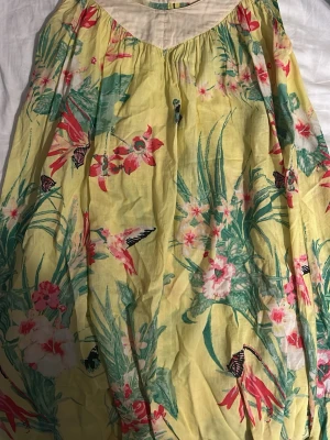 Gul blommig klänning från 365 SUNSHINE - Supersöt gul klänning med blommigt mönster och fjärilar från 365 SUNSHINE. Klänningen har en ljus krage, knappar i ryggen och är gjord i ett tunt, luftigt material. Perfekt för soliga dagar och ger en riktigt somrig vibe!