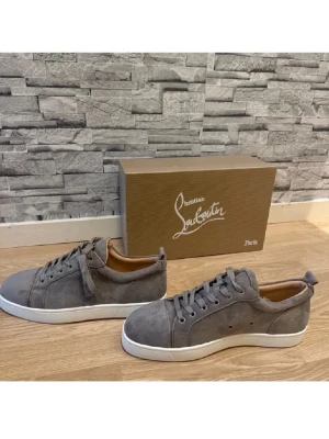 Grå mockasneakers från Christian Louboutin - Snygga grå sneakers i mocka från Christian Louboutin med klassisk röd sula och vita kanter. Skorna har rund tå, snörning och diskreta detaljer. Insidan är i ljust skinn och de har en clean, stilren look som passar till det mesta.