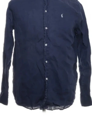 Mörkblå linne skjorta från Ralph Lauren - Klassisk mörkblå skjorta från Ralph Lauren med button-down krage och vita knappar framtill. Skjortan har lång ärm och den ikoniska loggan broderad på bröstet. Tillverkad i ett lätt och luftigt linnetyg, perfekt för en stilren look.