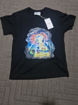 Svart t-shirt med tryck från Casablanca - Svart t-shirt från Casablanca Tennis Club med färgstarkt grafiskt tryck framtill som visar en surrealistisk öken med UFO och kaktusar. Klassisk passform och rund hals. Perfekt för dig som vill sticka ut med en unik tee.