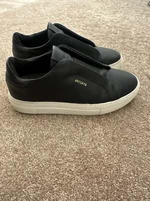 Svarta sneakers Axel Arigato - Ett par skor från Axel arigato. I storlek 40 i normal storlek. Använda 3-4 gånger och i perfekt skick. De är i äkta läder och laceless modellen så inga skosnören som behövs knytas. Nypris ligger på 2800kr