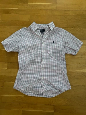 Rutig kortärmad skjorta Polo Ralph Lauren - Kortärmad skjorta från Polo Ralph Lauren i custom fit. Skjortan är vit med rött och blått rutmönster, klassisk krage och knappar framtill. Liten broderad logga på bröstet. Perfekt till sommaren för en clean och stilren look.