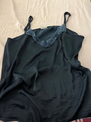 Mörkblå spetsdetaljerad linnetopp - Säljer en mörkblå linnetopp från Jacqueline de Yong i storlek 38. Toppen har tunna axelband och v-ringning med fina spetsdetaljer framtill. Materialet är mjukt och lätt, perfekt för varma dagar eller som lager under en kofta.