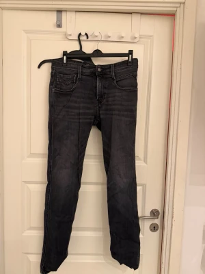 Replay Anbass svarta jeans slim fit - Säljer ett par Replay Anbass jeans i svart tvätt med snygga slitningar och klassiska fem fickor. Slim fit-modell med normal midja och raka ben. Jeansen är tillverkade i mjukt denimtyg och har Replay-logga på knapp och etikett.