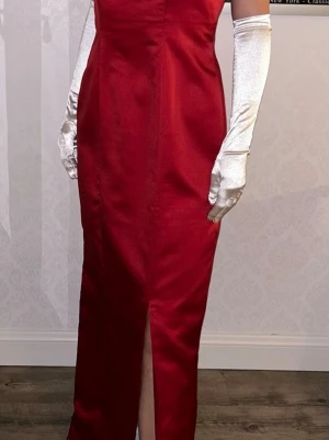 Hallonröd balklänning med slits - Snygg hallonröd långklänning i satinliknande material med smala axelband och har en ganska rak, figurnära passform. Klänningen passar it modellen, sitter därför löst över både byst,midja och höft. Färgen heter Bordeaux och är hallonröd. Klänningen har även innefoder och slits. Måtten på klänningen: Byst: 96, Midja: 86, Höft: 101. 
