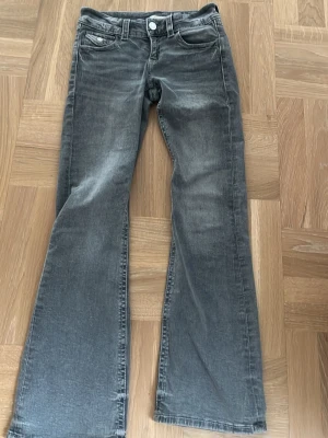 Grå bootcut jeans Gina Tricot 152 - Snygga grå jeans från Gina Tricot i storlek 152. Bootcut-modell med dekorativa detaljer och broderier på bakfickan. Klassisk femficksdesign och knapp med Gina Tricot-logga. Perfekta för dig som gillar en avslappnad men trendig look.