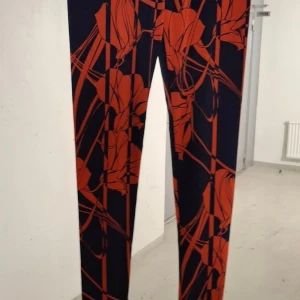 Svarta leggings med röd blommig print - Snygga svarta leggings med ett stort rött blommigt mönster. Tight passform och stretchigt material som sitter skönt. Perfekta för dig som vill sticka ut med en cool och färgstark look.
