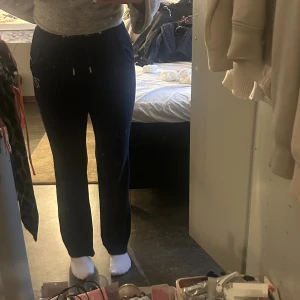 Juicy Couture marine blå velourbyxor - Marine blå mjukisbyxor från Juicy Couture i mjuk velour med snörning i midjan och glittrande Juicy-text baktill. Byxorna har raka ben och en strasslogga på ena benet. Perfekta för en chill och trendig look.