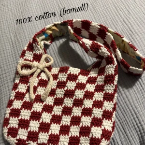 Virkad rutig röd och vit axelväska i bomull - Unik handgjord axelväska i 100% bomull med rödvitt rutigt mönster. Insidan har ett färgglatt tyg med motiv av svampar och växter. Väskan har en lång axelrem. Perfekt för dig som gillar retro och personliga accessoarer. Rosett ingår ej men jag kan göra en till dig om du vill. :)