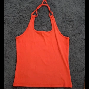 Orange ribbad linnetopp med knyt, M - Säljer en snygg orange linnetopp med ribbad struktur och knyt i nacken. Toppen har en rak passform och är ärmlös med halterneck-design. Perfekt för varma dagar och enkel att matcha med jeans eller kjol.