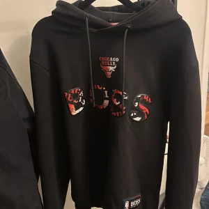 Hugo boss hoodie X Chicago Bulls NBA - Svart hoodie från Hugo Boss x NBA med Chicago Bulls-tryck och stor BOSS-logga framtill. Tröjan har huva med snörning. Väldigt bra skick!
